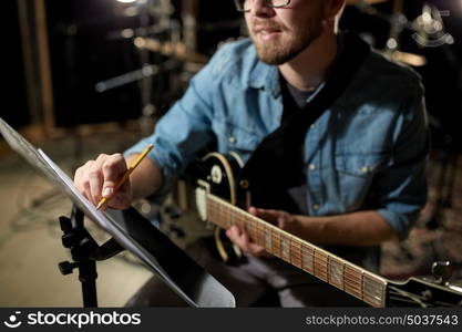 people, art and entertainment concept - man with guitar writing notes to music book at studio. man with guitar writing to music book at studio