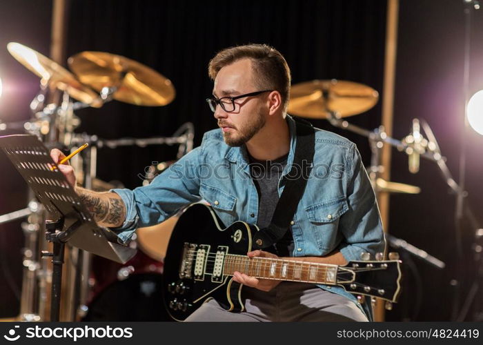 people, art, composition and entertainment concept - man with guitar writing lyrics or notes to music book at studio. man with guitar writing to music book at studio