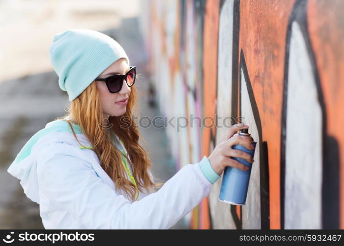 people, art, creativity and youth culture concept - young woman or teenage girl drawing graffiti with spray paint on street wall