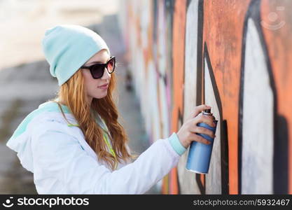 people, art, creativity and youth culture concept - young woman or teenage girl drawing graffiti with spray paint on street wall