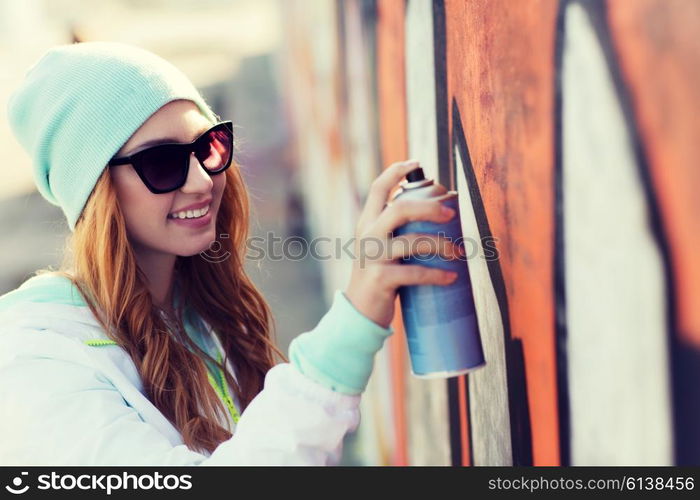 people, art, creativity and youth culture concept - young woman or teenage girl drawing graffiti with spray paint on street wall