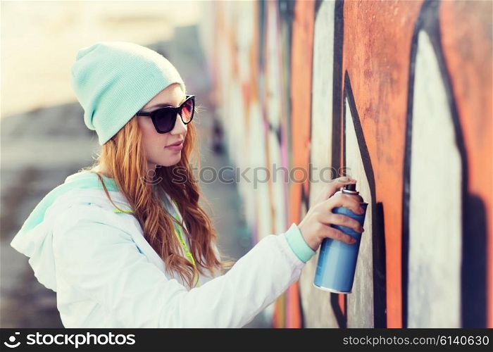 people, art, creativity and youth culture concept - young woman or teenage girl drawing graffiti with spray paint on street wall