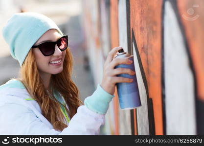 people, art, creativity and youth culture concept - young woman or teenage girl drawing graffiti with spray paint on street wall