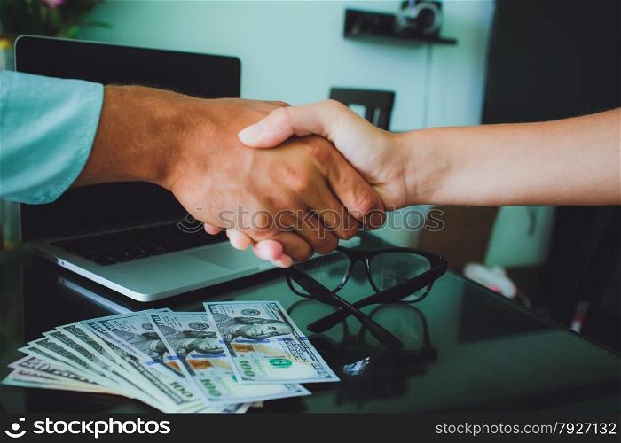People at work: man and woman hand shaking at a meeting. Closeup shot of a two businesspeople shaking hands, glasses , money, laptop on background.