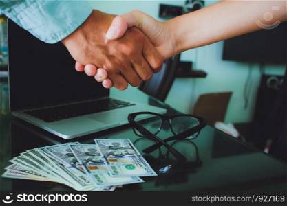 People at work: man and woman hand shaking at a meeting. Closeup shot of a two businesspeople shaking hands, glasses , money, laptop on background.