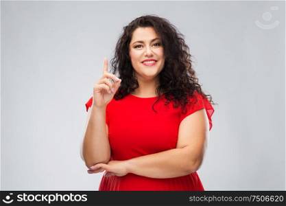 people, attention and idea concept - happy woman in red dress pointing finger up over grey background. happy woman in red dress pointing finger up