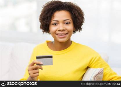 people, bank, shopping and e-money concept - happy african american young woman sitting on sofa with credit or debit card at home