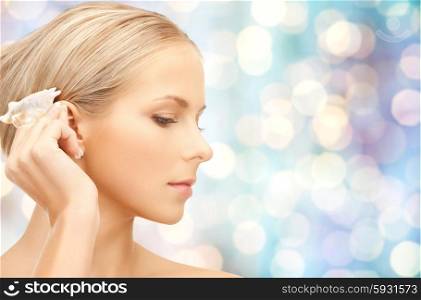 people, beauty and beach concept - beautiful woman with seashell over blue holidays lights background