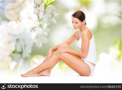 people, beauty and body care concept - beautiful woman in cotton underwear touching legs over green natural cherry blossom background