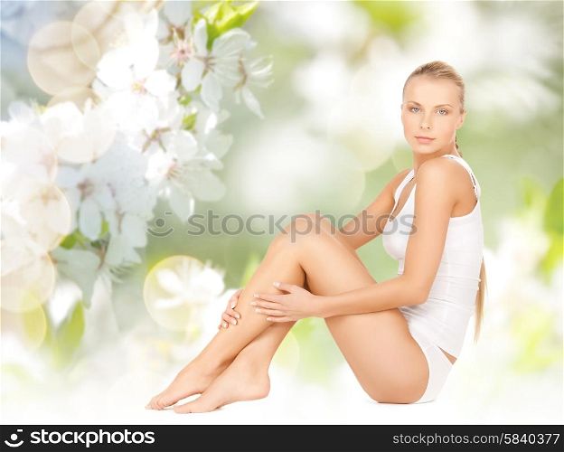 people, beauty and body care concept - beautiful woman in cotton underwear touching legs over green natural cherry blossom background