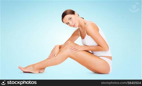 people, beauty and body care concept - beautiful woman in cotton underwear touching legs over blue background