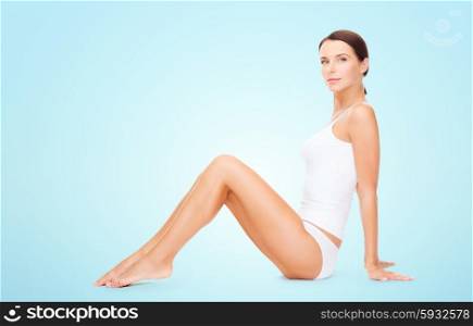 people, beauty and body care concept - beautiful woman in cotton underwear showing her legs over blue background