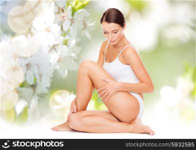 people, beauty and body care concept - beautiful woman in cotton underwear touching her hips over green natural cherry blossom background