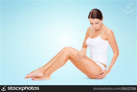 people, beauty and body care concept - beautiful woman in cotton underwear touching her hips over blue background