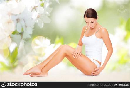 people, beauty and body care concept - beautiful woman in cotton underwear touching her hips over green natural cherry blossom background