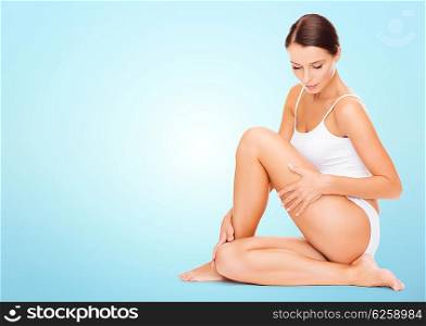 people, beauty and body care concept - beautiful woman in cotton underwear touching her hips over blue background