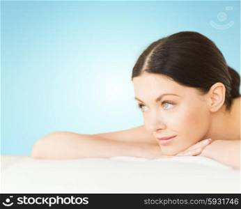 people, beauty and body care concept - happy beautiful woman lying on massage desk at spa over blue background