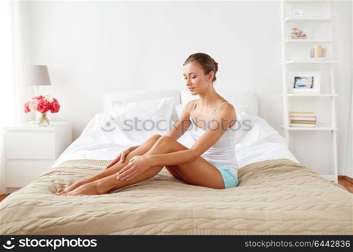 people, beauty and bodycare concept - beautiful woman with bare legs sitting on bed at home bedroom. beautiful woman with bare legs on bed at home
