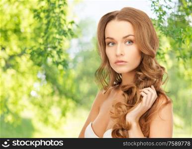 people, beauty and hair care concept - beautiful woman over green natural background. beautiful woman with curly hair