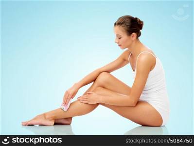people, beauty and hair removal concept - beautiful woman with epilator removing hair from legs sitting on floor over blue background. woman with epilator removing hair on legs. woman with epilator removing hair on legs