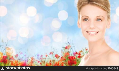 people, beauty and health care concept - close up of smiling young woman over blue lights and poppy field background