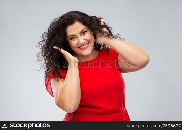 people, beauty and portrait concept - happy woman in red dress touching her hair over grey background. happy woman touching her hair over grey background