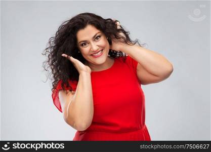 people, beauty and portrait concept - happy woman in red dress touching her hair over grey background. happy woman touching her hair over grey background