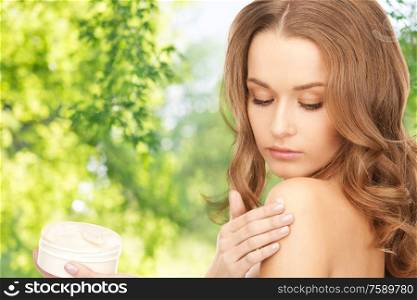 people, beauty and skin care concept - beautiful woman applying body cream to her shoulder over green natural background. woman applying body cream to her shoulder