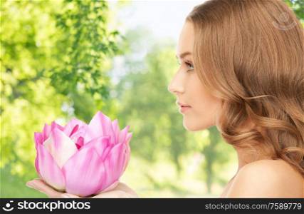 people, beauty and skin care concept - beautiful woman with pink lotus flower over green natural background. beautiful woman with pink lotus flower