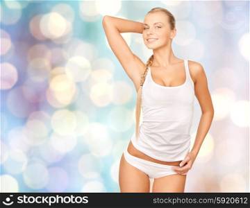 people, beauty, body care and fashion concept - happy beautiful young woman in cotton underwear posing over blue holidays lights background