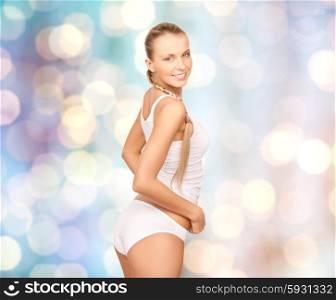 people, beauty, body care and fashion concept - happy beautiful young woman in cotton underwear over blue holidays lights background