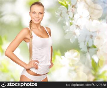 people, beauty, body care and health concept - happy beautiful young woman in cotton underwear over green cherry blossom background