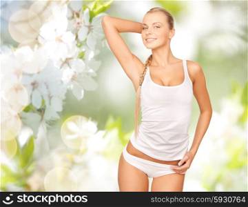 people, beauty, body care and health concept - happy beautiful young woman in cotton underwear posing over green cherry blossom background