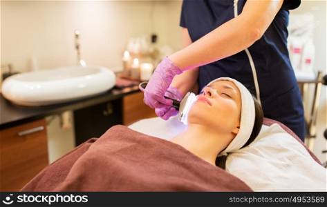 people, beauty, cosmetic treatment, cosmetology and technology concept - beautician with microdermabrasion device doing face exfoliation to young woman lying at spa parlor. young woman having face microdermabrasion at spa