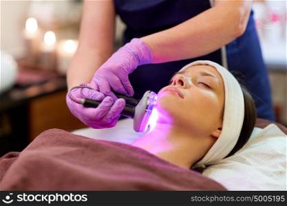 people, beauty, cosmetic treatment, cosmetology and technology concept - beautician with microdermabrasion device doing face exfoliation to young woman lying at spa. young woman having face microdermabrasion at spa