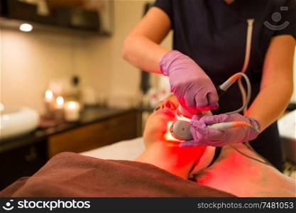 people, beauty, cosmetic treatment, cosmetology and technology concept - beautician with microdermabrasion device doing face exfoliation to woman lying at spa. young woman having face microdermabrasion at spa