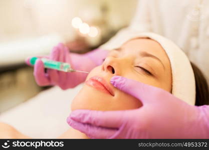 people, beauty, cosmetology and technology concept - beautician with syringe doing hyaluronic acid injection for lip augmentation to young woman. beautician doing beauty injection to woman lips