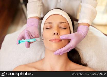 people, beauty, cosmetology and technology concept - beautician with syringe doing hyaluronic acid injection for lip augmentation to young woman. beautician doing beauty injection to woman lips