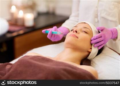 people, beauty, cosmetology and technology concept - beautician with syringe doing hyaluronic acid injection for lip augmentation to young woman. beautician doing beauty injection to woman lips