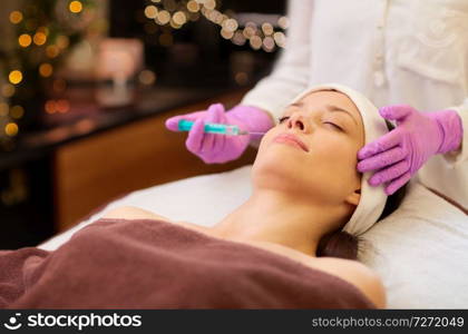 people, beauty, cosmetology and technology concept - beautician with syringe doing hyaluronic acid injection for lip augmentation to young woman. beautician doing beauty injection to woman lips