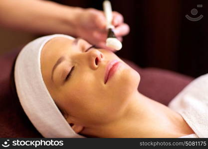 people, beauty, cosmetology and treatment concept - close up of beautiful young woman lying with closed eyes and cosmetologist applying facial mask by brush at spa. beautician applying facial mask to woman at spa