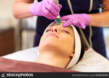 people, beauty, cosmetology, exfoliation and technology concept - beautiful young woman having microdermabrasion facial treatment with crystals in spa. woman having microdermabrasion facial treatment