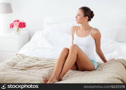 people, beauty, depilation, epilation and bodycare concept - beautiful woman with bare legs sitting on bed at home bedroom. beautiful woman with bare legs on bed at home