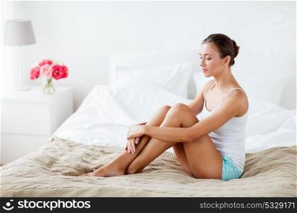 people, beauty, depilation, epilation and bodycare concept - beautiful woman with bare legs sitting on bed at home bedroom. beautiful woman with bare legs on bed at home