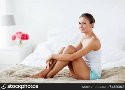 people, beauty, depilation, epilation and bodycare concept - beautiful woman with bare legs sitting on bed at home bedroom. beautiful woman with bare legs on bed at home