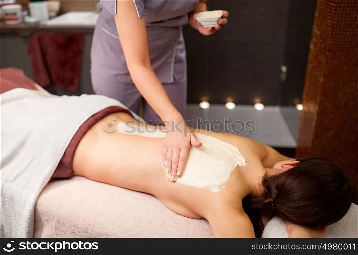people, beauty, healthy lifestyle and relaxation concept - beautiful young woman lying and having back massage with cream at spa. woman having back massage with cream at spa