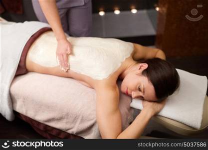 people, beauty, healthy lifestyle and relaxation concept - beautiful young woman lying and having back massage with cream at spa. woman lying and having back massage at spa