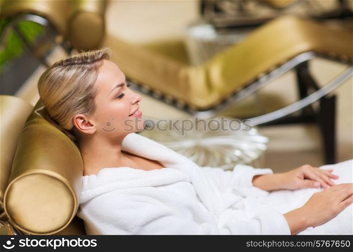 people, beauty, healthy lifestyle and relaxation concept - beautiful young woman lying on chaise-longue in bath robe at spa