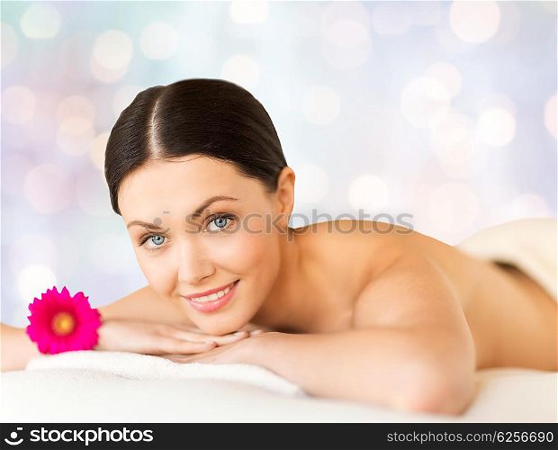 people, beauty, holidays and body care concept - happy beautiful woman lying on massage desk at spa over blue lights background
