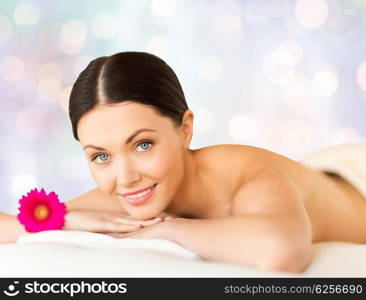 people, beauty, holidays and body care concept - happy beautiful woman lying on massage desk at spa over blue lights background